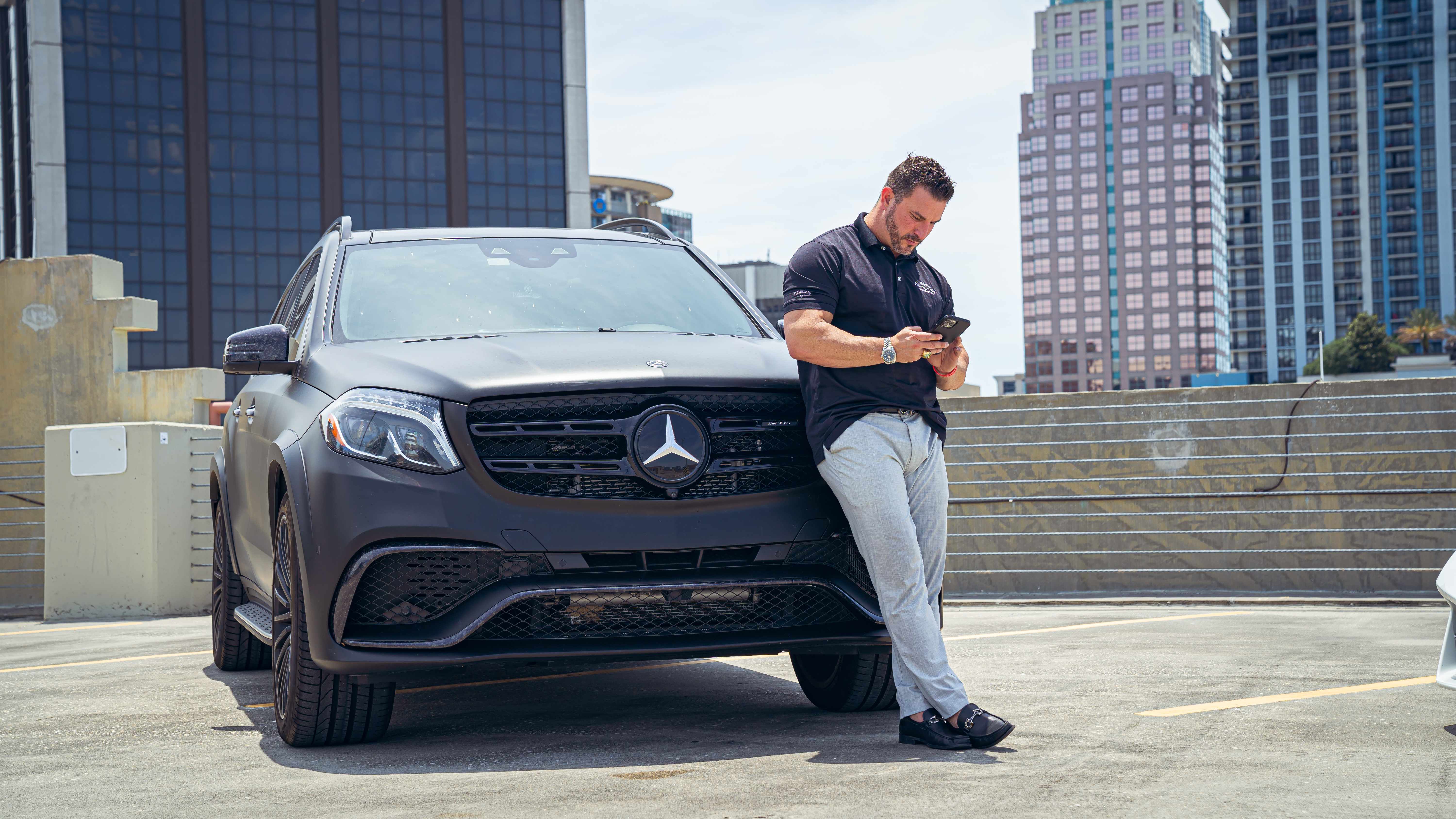 Man checking phone leaning against Mercedes GLS