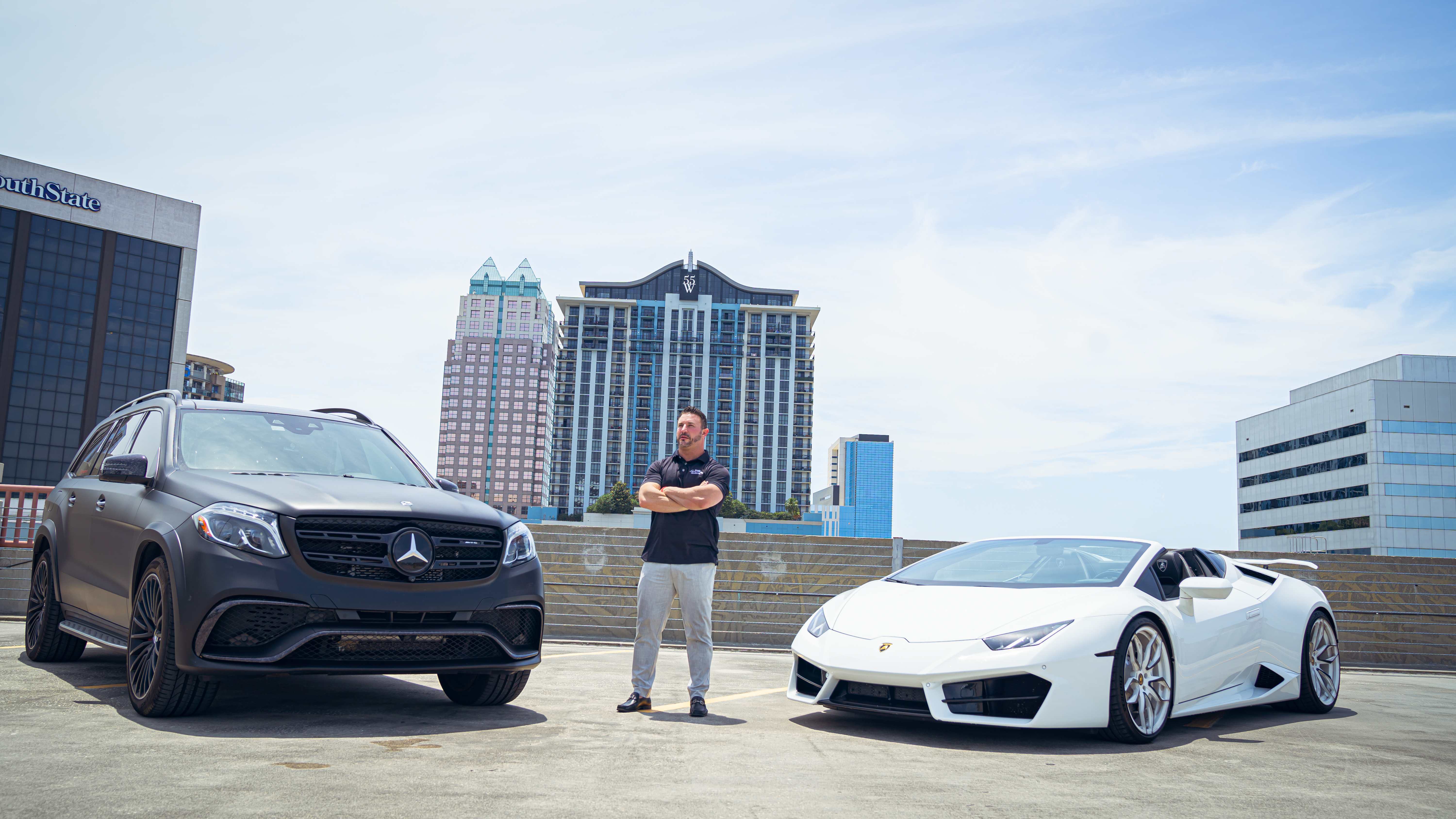 Man posing between luxury vehicles on city rooftop
