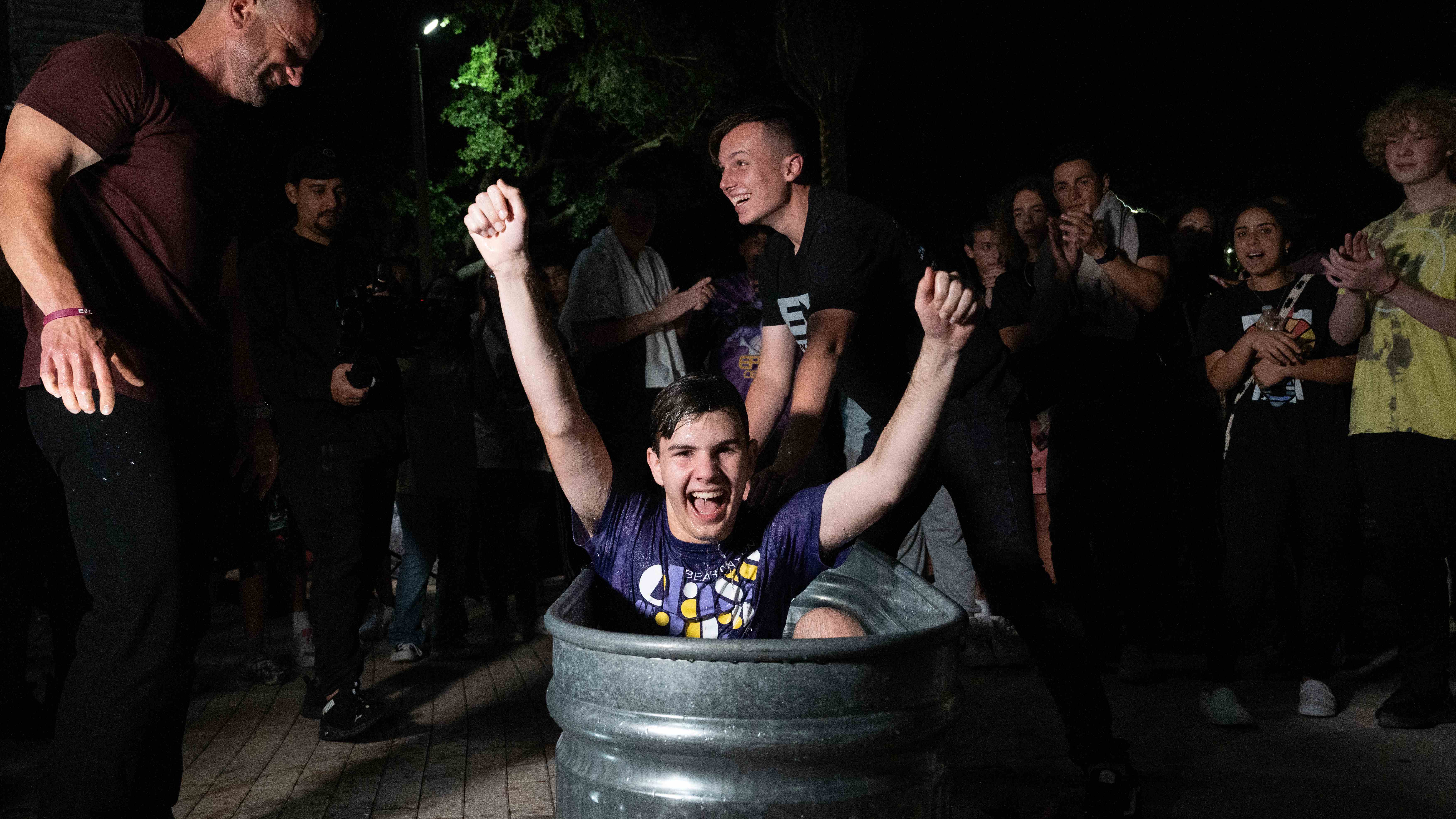 Joyful outdoor baptism moment with teen celebrating in tub surrounded by cheering crowd