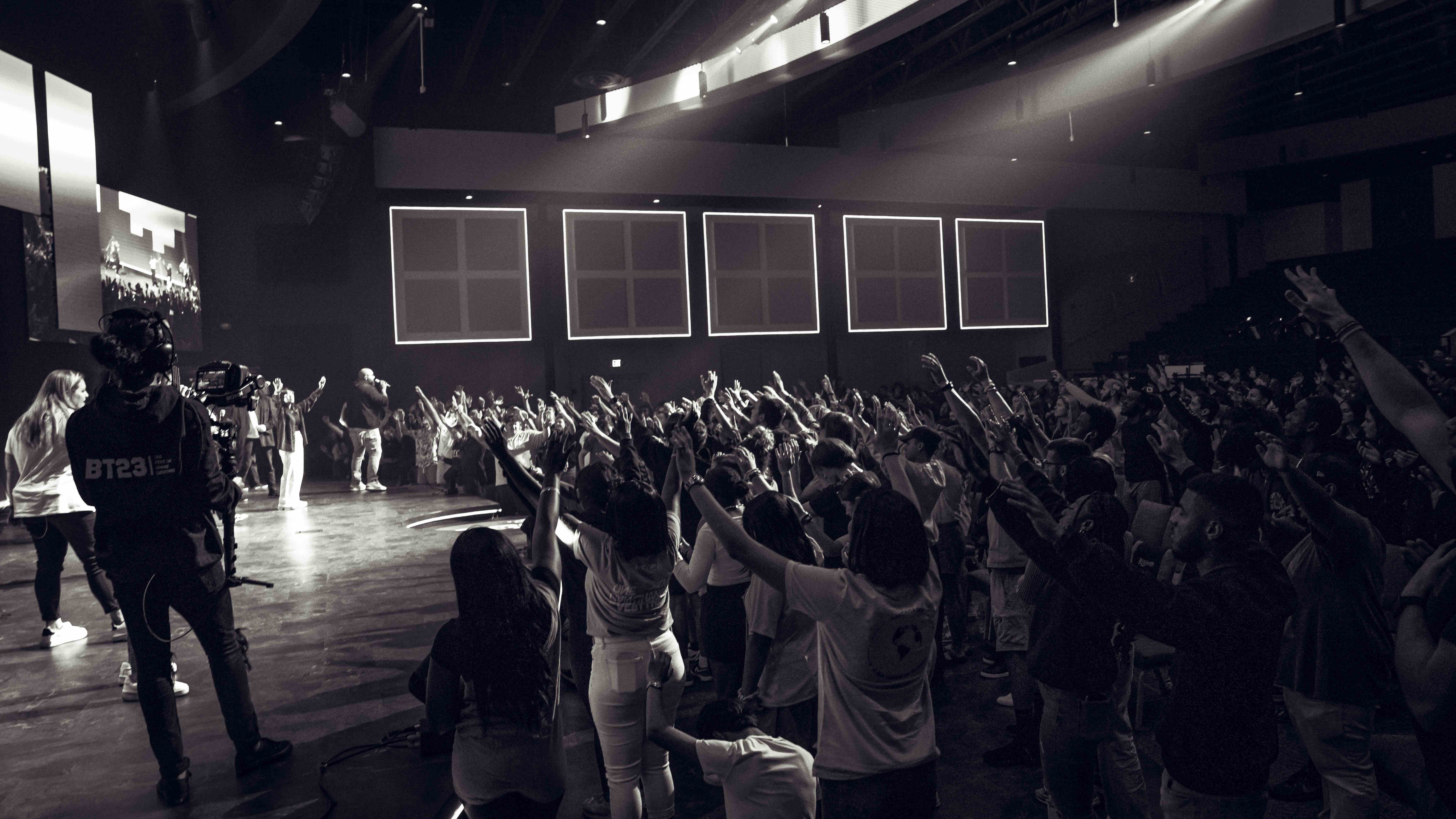 Cameraman filming worship service with congregation hands raised, black and white