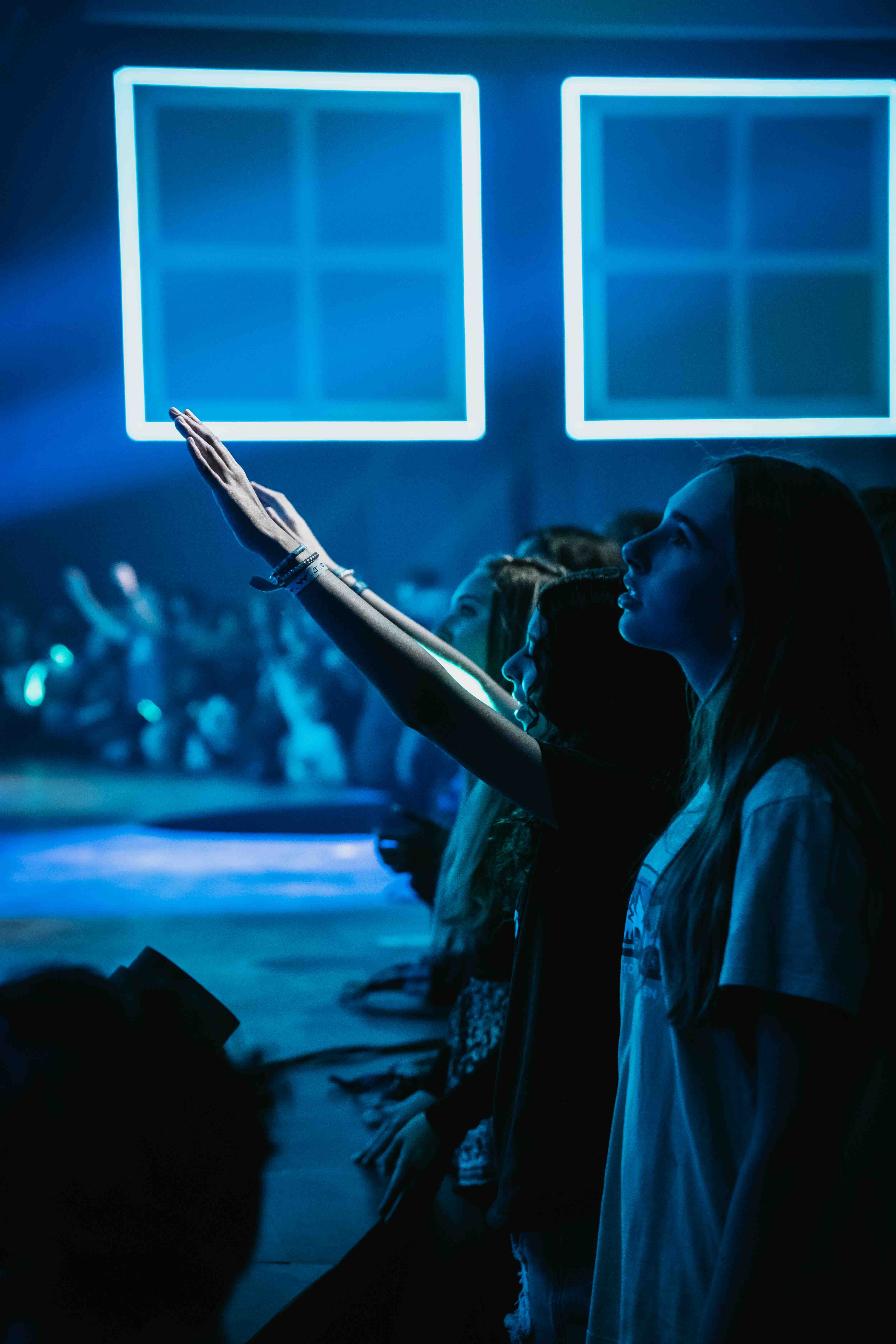 Young woman with hand raised in worship under blue neon lights