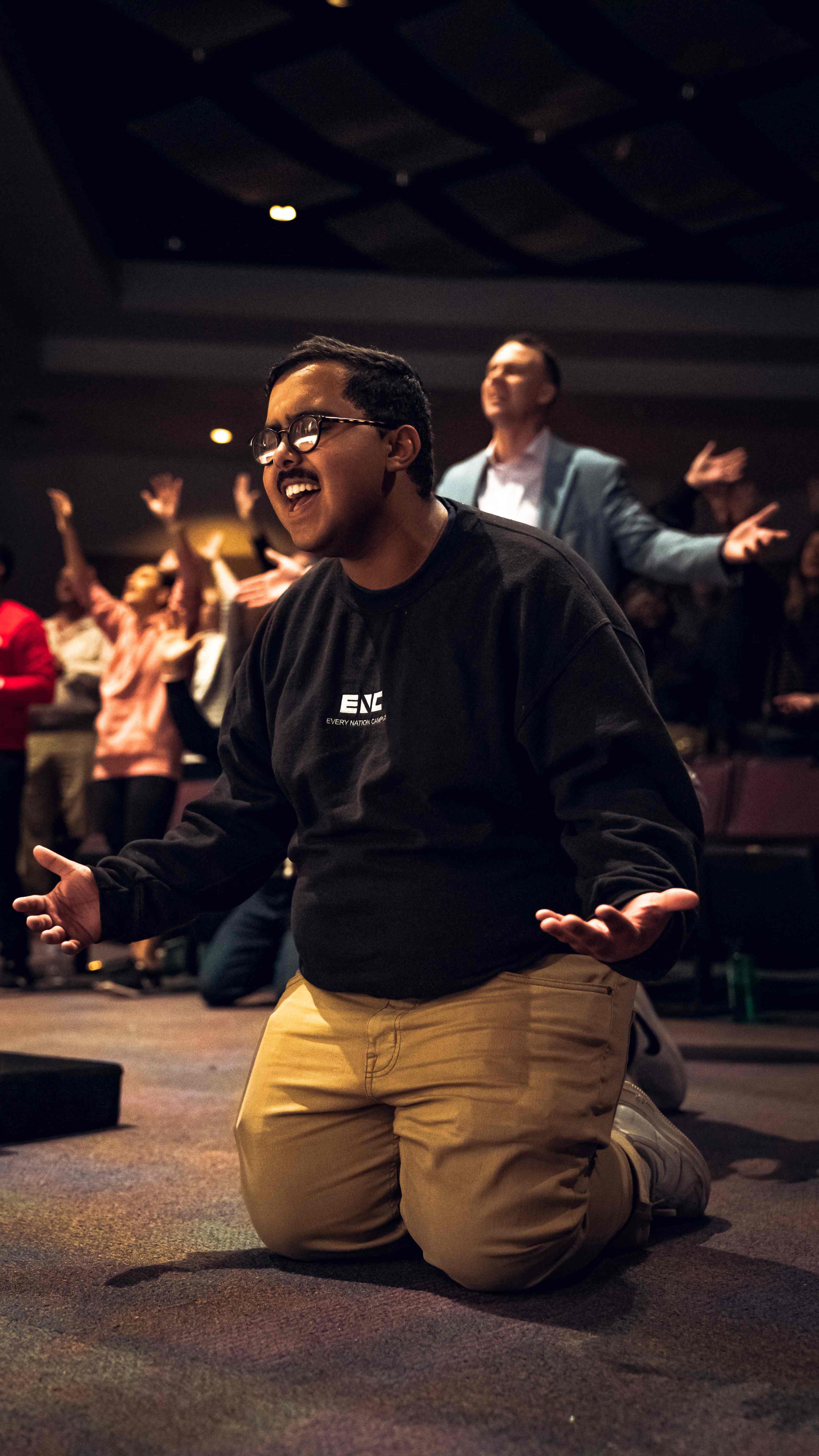 Young man in Every Nation Campus sweatshirt kneeling in worship