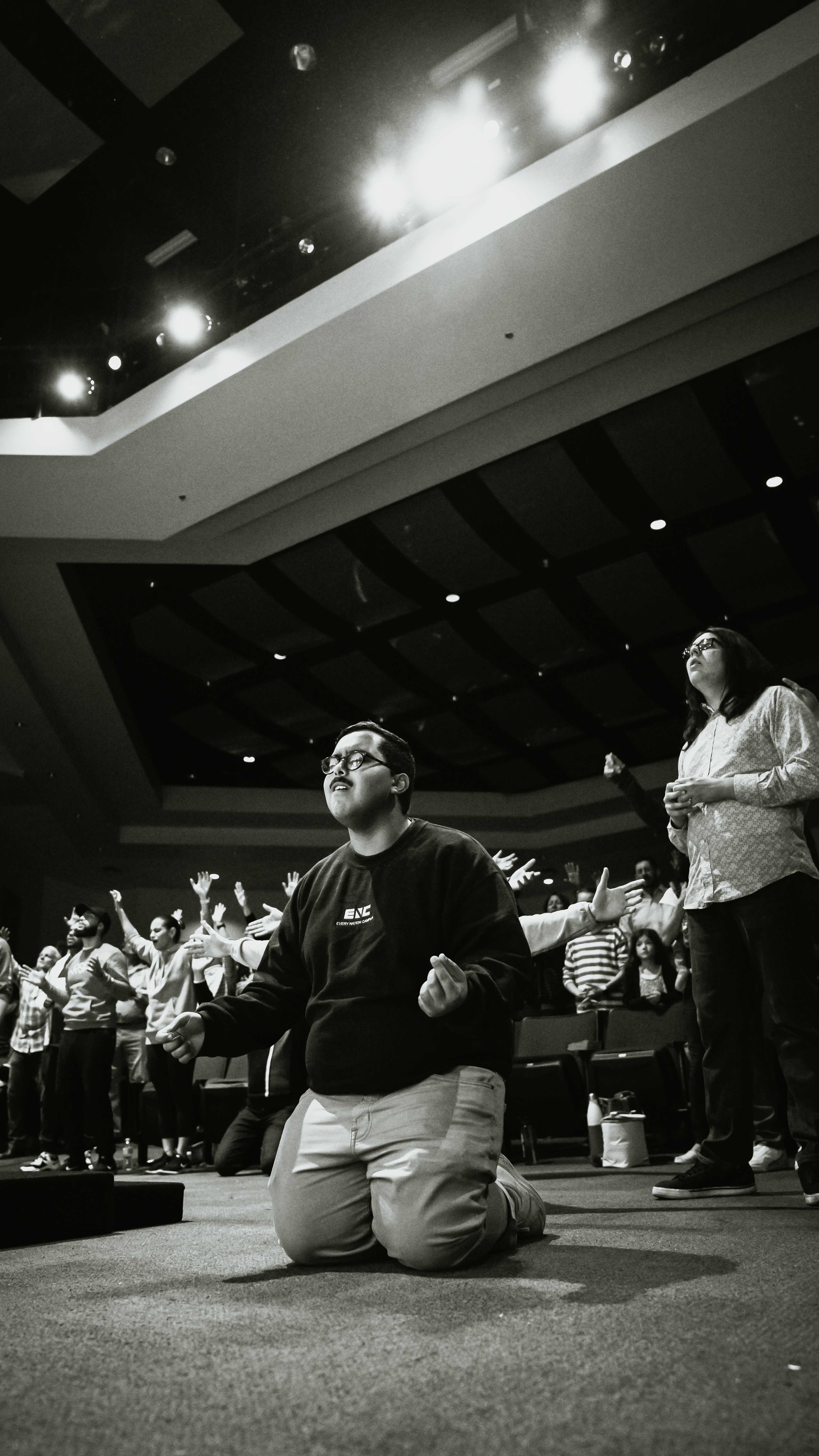 Young man kneeling in worship with congregation behind, black and white