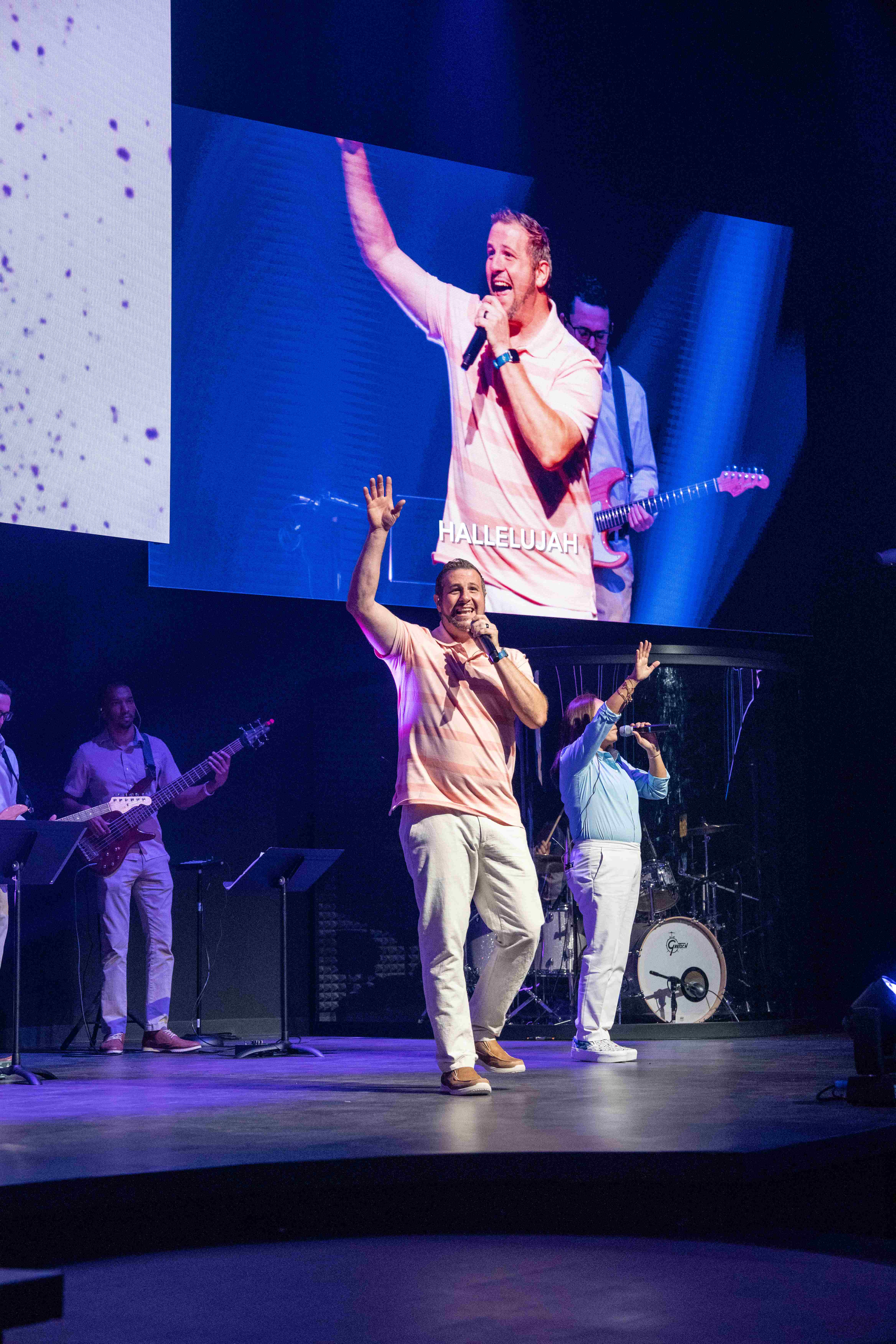 Pastor leading worship on stage with 'Hallelujah' on screens behind