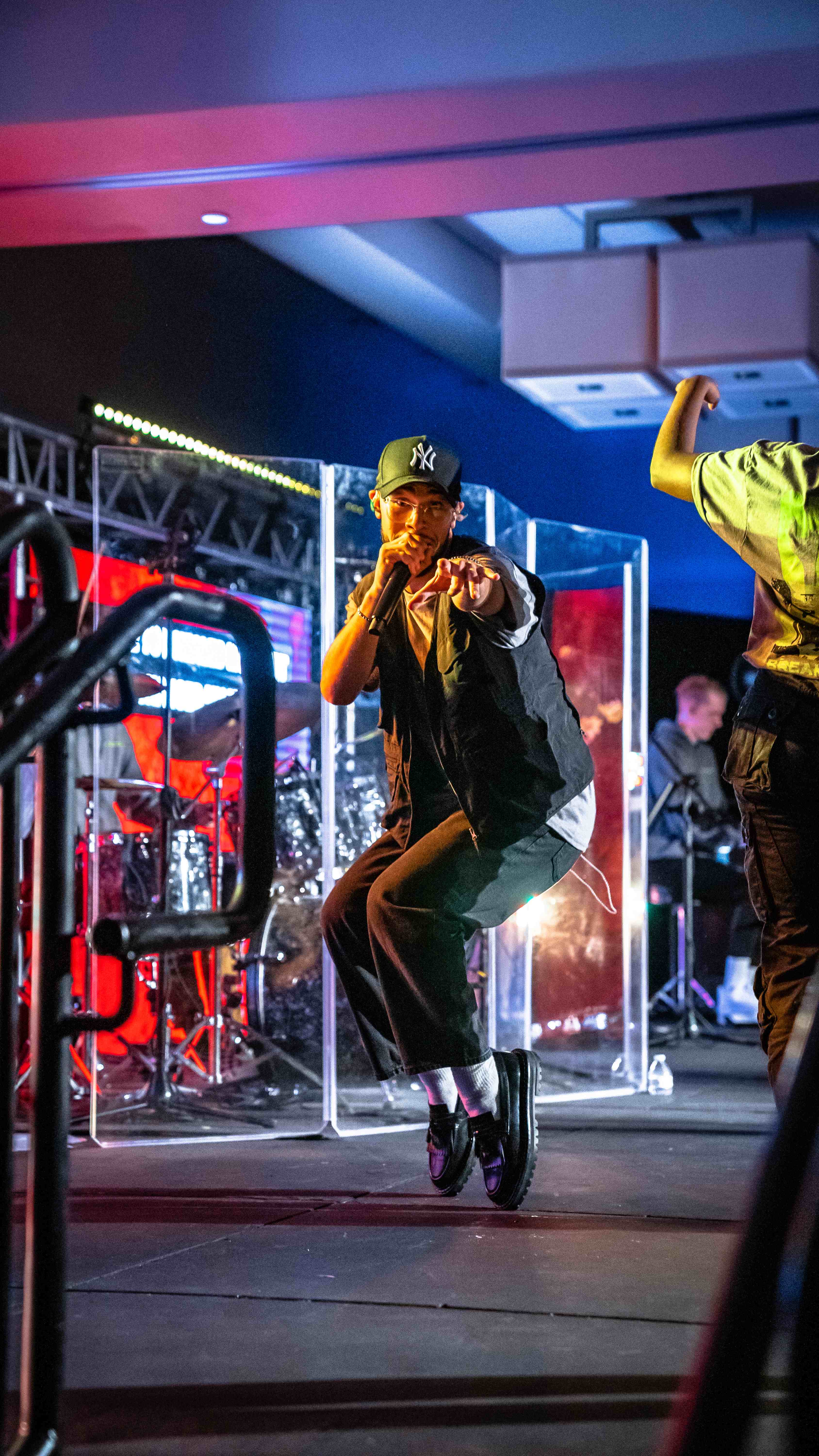 Performer in NY cap singing on stage with colorful lighting behind