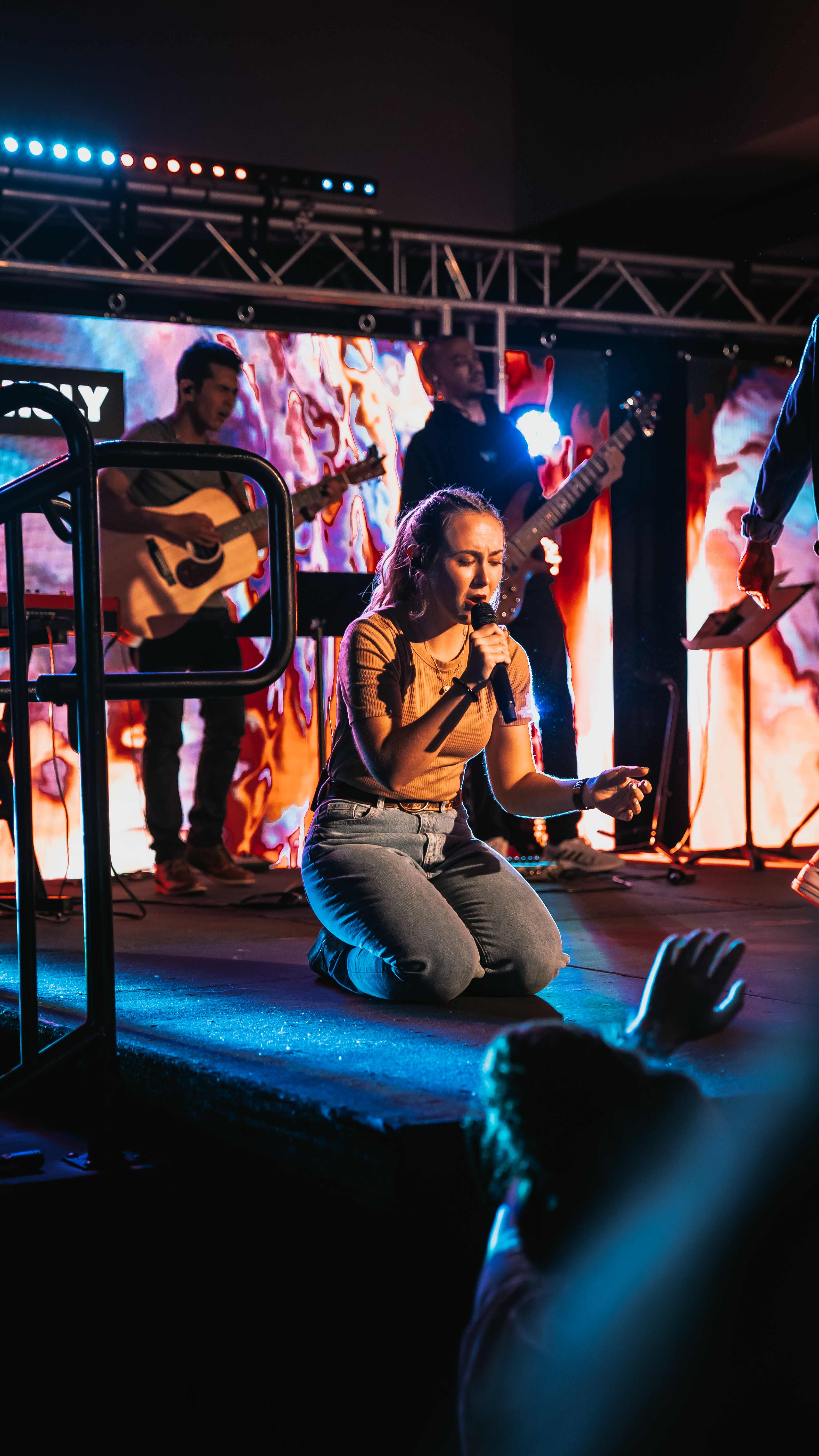 Female singer kneeling on stage with fire visuals on screens behind