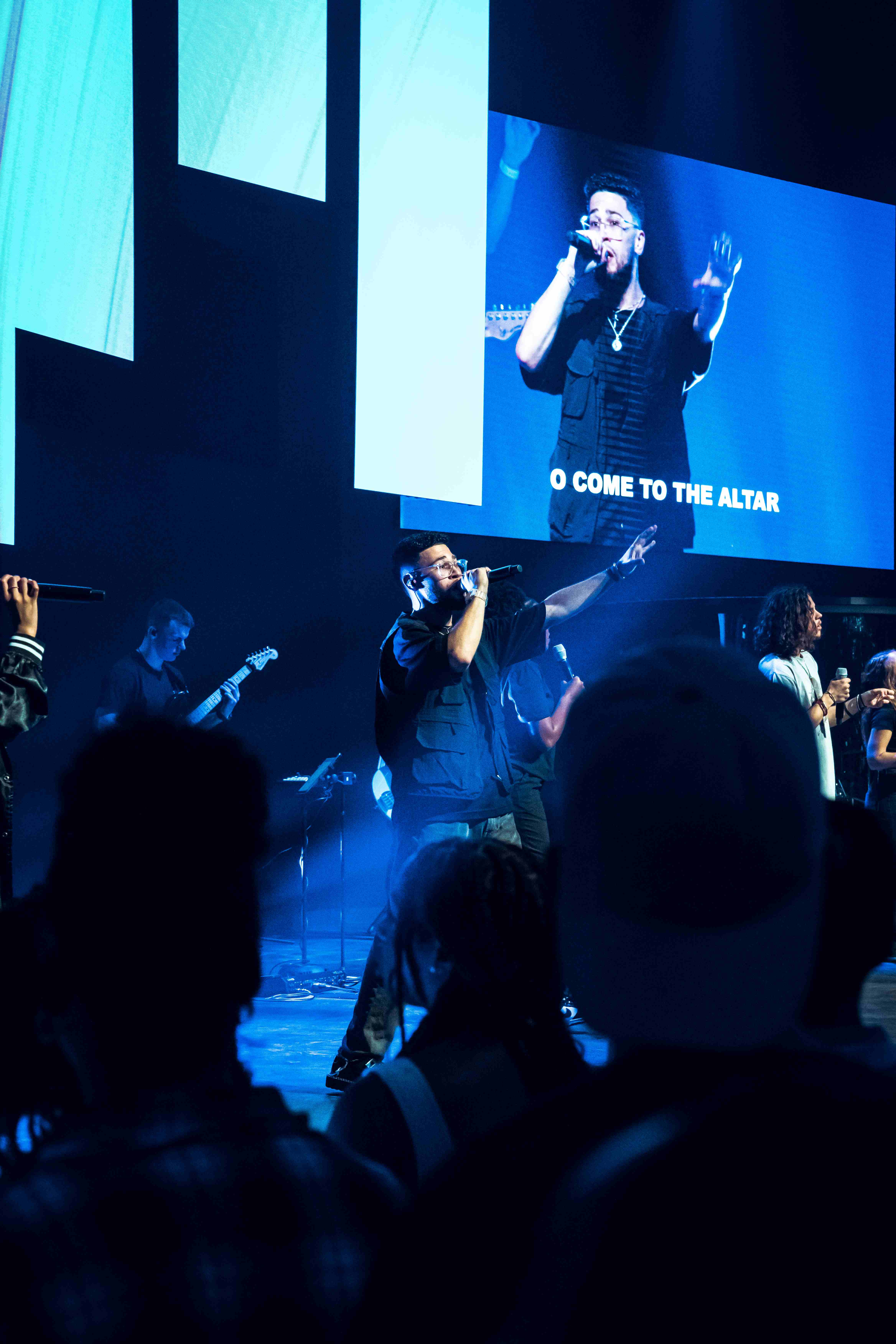 Worship leader singing 'O Come to the Altar' with band and blue lighting