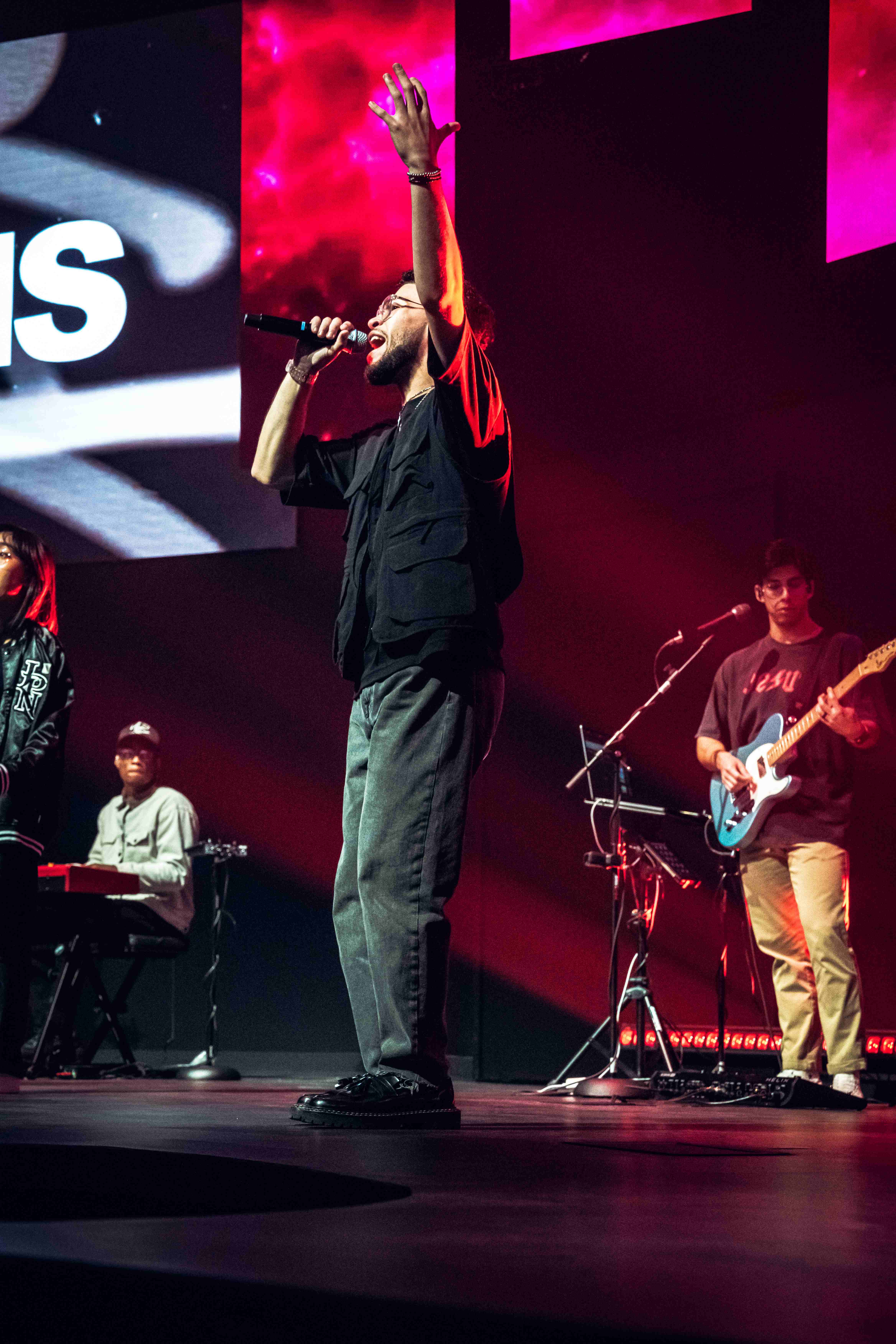 Worship leader with arm raised, red and pink stage backdrop with band