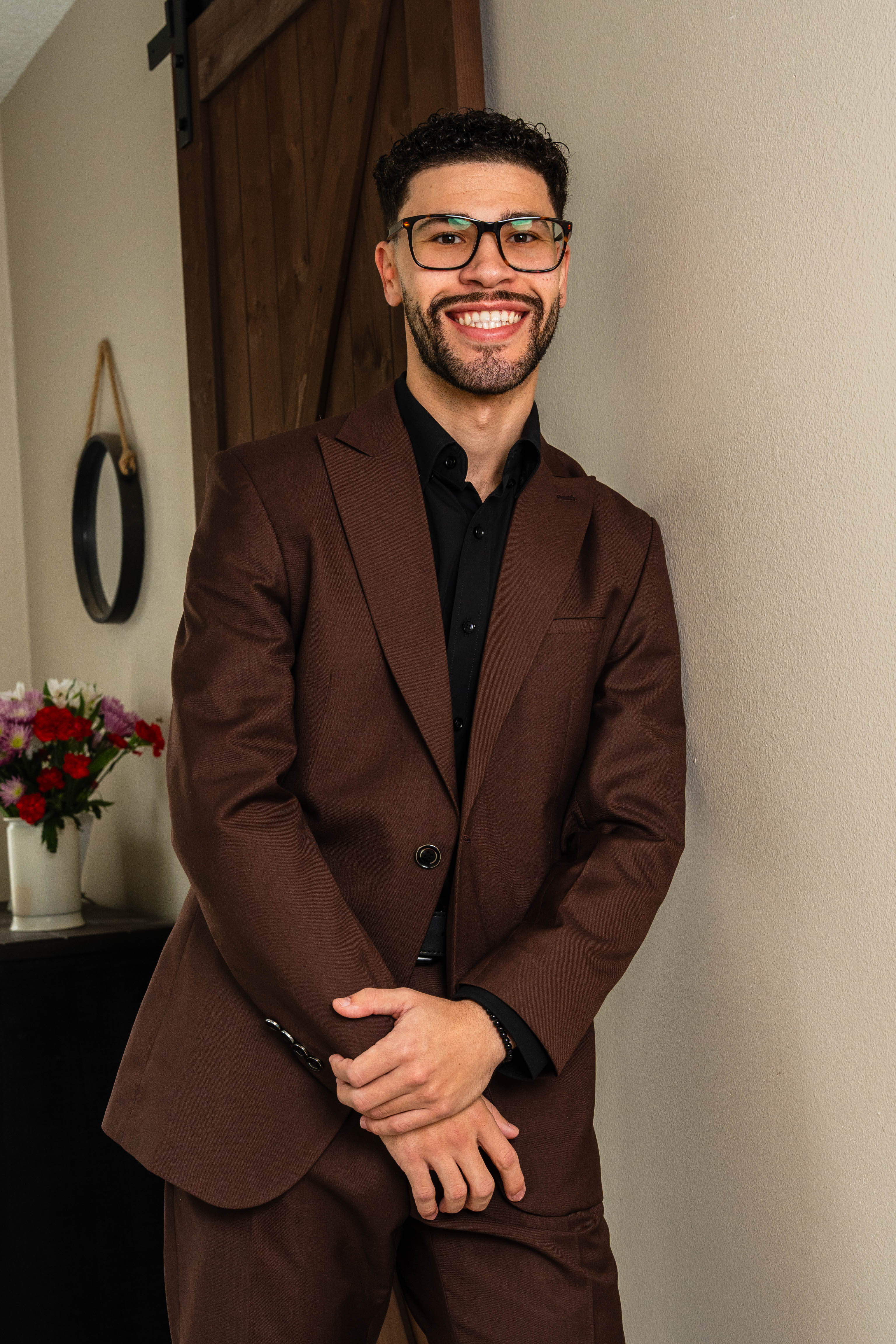 Groom smiling confidently in brown suit and glasses